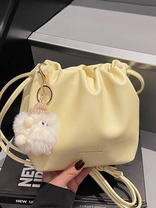 Pale yellow drawstring bucket bag with plush charm and fashion text in close-up view