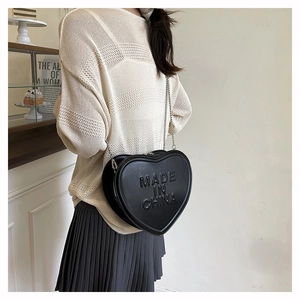 Detail of a black heart-shaped crossbody bag featuring embossed lettering and silver chain