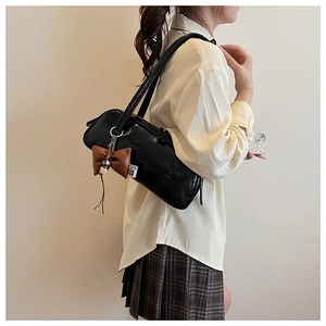 Detail of black glossy PU leather bowling bag with vintage brown bow charm and slim strap