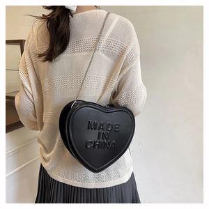 Detail of black heart-shaped crossbody bag with embossed lettering and fine chain strap