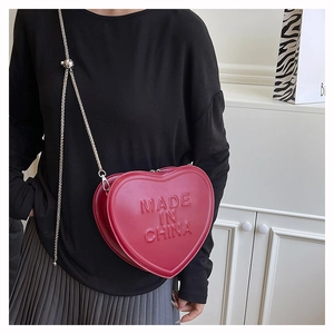 Detail of red heart-shaped leather crossbody bag with embossed lettering and metal chain