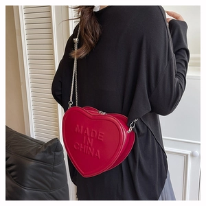 Detail of red heart-shaped crossbody bag with embossed lettering and metal chain strap