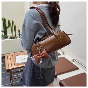 Brown glossy leather cylindrical Boston bag with bow tassel detail on a fashion model