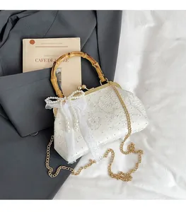 Detail of white lace clutch featuring bamboo handle and elegant pearl charm fringe