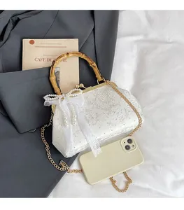 Detail of white floral lace clutch bag featuring bamboo handle and pearl bow accent