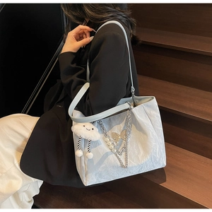Dettaglio della borsa tote azzurra con trama ondulata, catena di perle e ciondolo nuvola