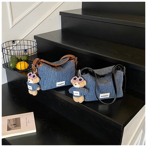 Detail of denim crossbody bags with leather trim and bear charms on a wooden staircase