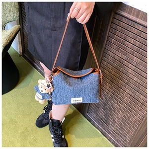 Blue denim shoulder bag detail featuring brown leather trim and cute teddy bear charm