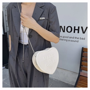 Macro detail of white heart-shaped leather crossbody bag with embossed lettering
