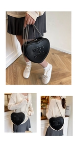 Detail of heart-shaped black crossbody bag featuring embossed lettering and chain strap