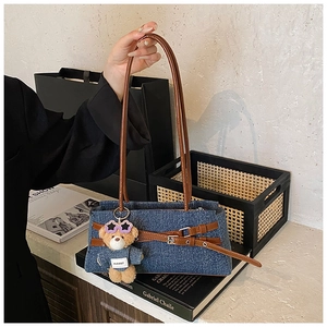 Detail of dark blue denim tote with brown leather straps and cute bear charm pendant