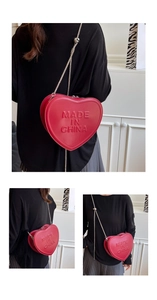 Detail view of a red heart-shaped crossbody bag with embossed text and silver chain