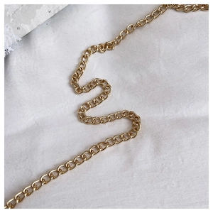 Macro detail of glossy golden metal chain strap on textured fabric for shell bag