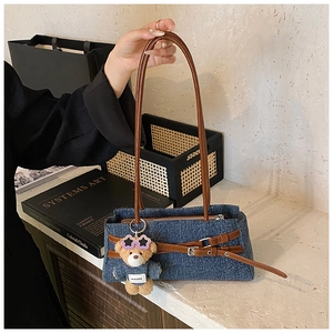 Detail of blue denim shoulder bag with brown leather straps and teddy bear charm