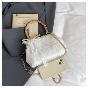 Detailed view of white lace handbag featuring a bamboo handle and pearl bow charm