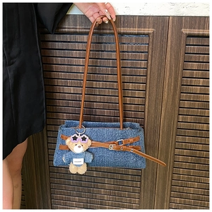 Blue denim baguette bag with brown leather straps and a stylish teddy bear pendant detail