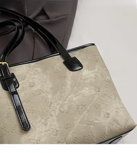 Detail view of beige tote bag with black trim and embossed cartoon bear patterns