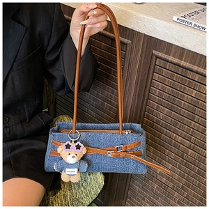 Detail of blue denim shoulder bag with brown leather straps and plush bear charm
