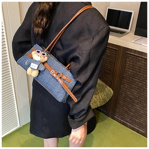 Blue denim shoulder bag featuring a cute teddy bear charm and brown leather straps