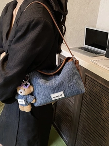 Blue denim crossbody bag with brown leather strap and cute bear charm in casual office setting