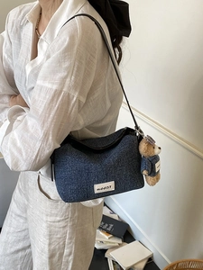 Vintage denim shoulder bag with leather strap and cute bear pendant on white background