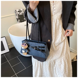 Blue denim tote bag detail featuring a cute teddy bear charm and black leather straps