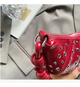Detail of red leather bag showing silver rivets and knotted handle on a stylish background