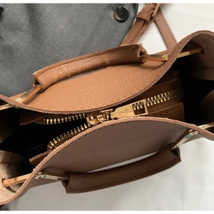 Detail of tan pebble leather handbag with gold metal handle and zip closure