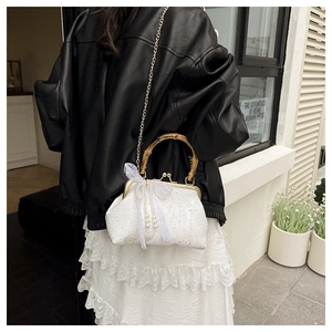 Detail of white lace evening bag with bamboo handle and pearl bow charm on black leather jacket