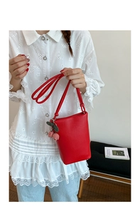 Detail of red lychee leather bucket bag with cherry charm and logo on lace shirt
