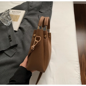 Detailed close-up of brown litchi grain leather handbag with gold metal hardware