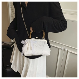 Detail of white lace shell bag with bamboo handle, oversized bow and pearl tassel decor