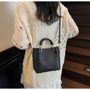Close-up of black lychee leather crossbody bag with golden hardware on a stylish model
