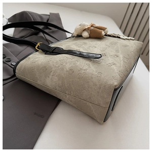 Detail of embossed tote bag with bear patterns, black leather straps and plush charm