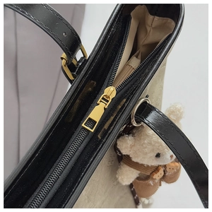 Detail of gold zipper closure on tote bag with black leather trim and cute bear charm