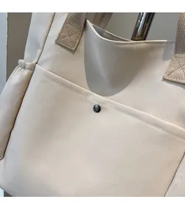 Detail of canvas tote bag showing front magnetic snap pocket and reinforced stitching
