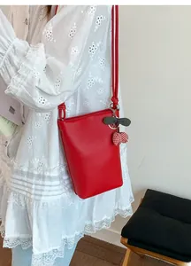 Red pebbled leather bucket bag styled with a cherry charm on a model in a white dress
