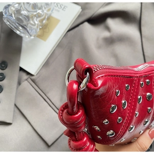 Close-up of red pleated leather handbag featuring silver rivets and knotted handle detail