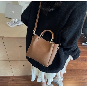 Detail of brown litchi pattern leather handbag with golden hardware and adjustable strap