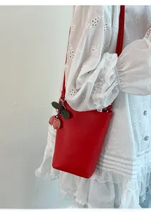 Detail of red bucket bag with lychee texture and cherry charm on a lace dress