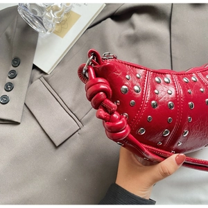 Close-up of red crescent bag featuring silver studs and hand-braided leather strap details