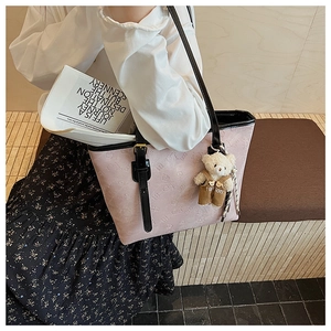 Detail of pink embossed tote bag with slim black straps and a cute plush bear charm