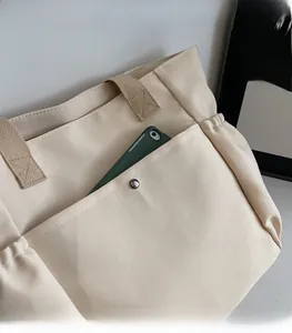 Detail of canvas tote bag showing wide strap and front pocket with silver metal snap