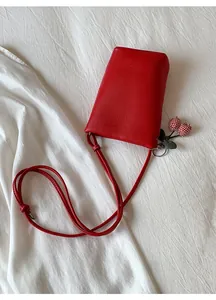 Red litchi grain leather crossbody phone bag with cherry pendant on white fabric