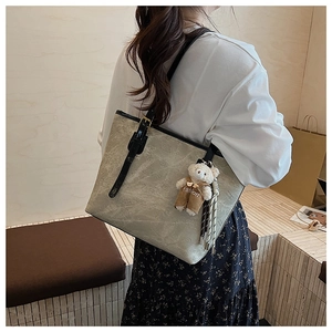 Detailed view of green embossed tote bag with cute bear doll charm on black strap