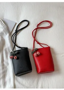 Detail view of small lychee grain leather crossbody bags in black and red with cherry charm
