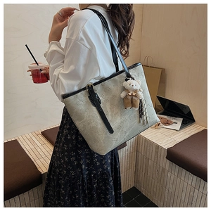 Detail of beige tote bag with embossed pattern, featuring a cute bear charm and long tassels