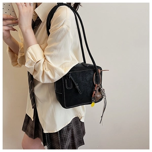 Detail of black leather tote bag with contrast stitching and brown charm on long straps