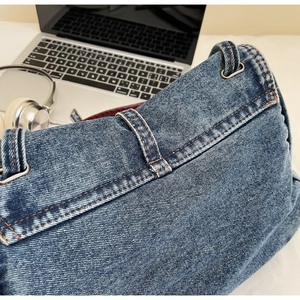 Gros plan du sac en jean bleu délavé avec surpiqûres orange et boucles métalliques argentées