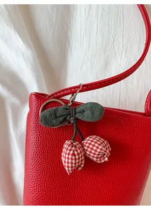 Detail of cherry fabric bag charm with green bow and red plaid pattern on leather bag